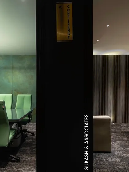A view into two distinct yet connected spaces. On the left, a conference room with vibrant green chairs against a textured wall, and on the right, an executive office with warm wood paneling, showcasing our ability to create varied moods within a cohesive design.