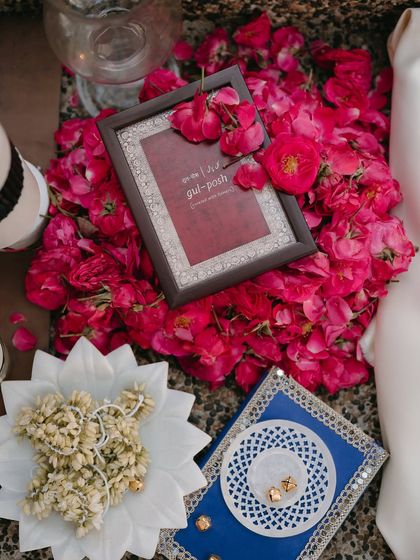 A flat lay of beautiful details, including fresh rose petals, jasmine gajras, and framed Urdu calligraphy.
