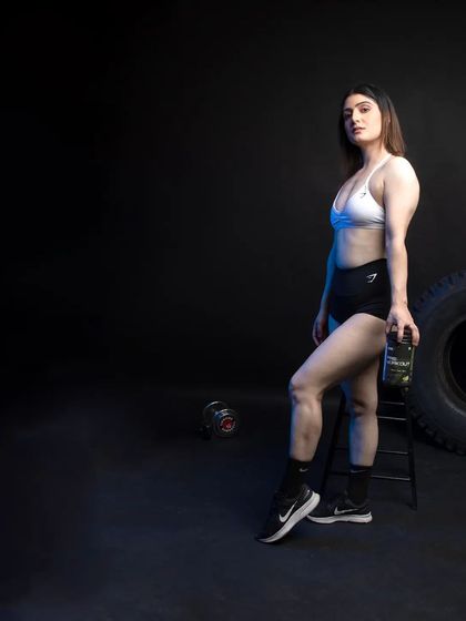 A profile shot of the model with a different product from the line. The composition uses dramatic side lighting to sculpt the model's physique and highlight the product she is holding, creating a sleek and modern look.