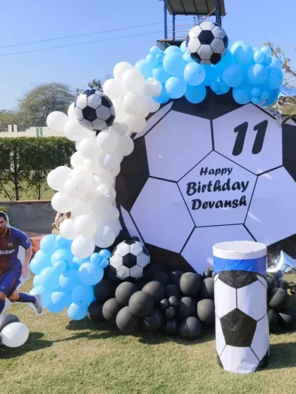 A fantastic outdoor football party for an 11th birthday. The decor features a giant football backdrop, a Messi cutout, and a blue, white, and black balloon arrangement.