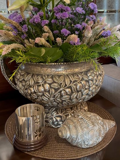 An ornate silver vessel holding a beautiful arrangement of purple and white flowers. We pay close attention to the vases and containers we use, as they are an important part of the overall design.