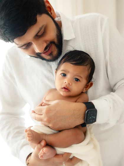 A proud father holding his newborn, who looks directly at the camera. Capturing these moments of eye contact is so special in the early days.