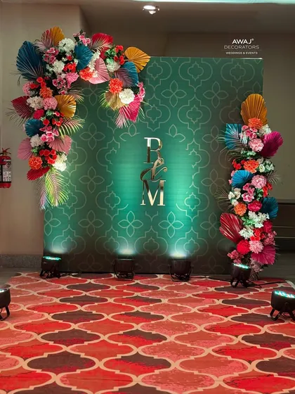 The Mehendi photo booth, featuring a green patterned backdrop, the couple's initials, and an explosion of colorful flowers.