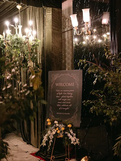 A welcome sign for a grand evening event, framed by lush greenery and elegant chandeliers.