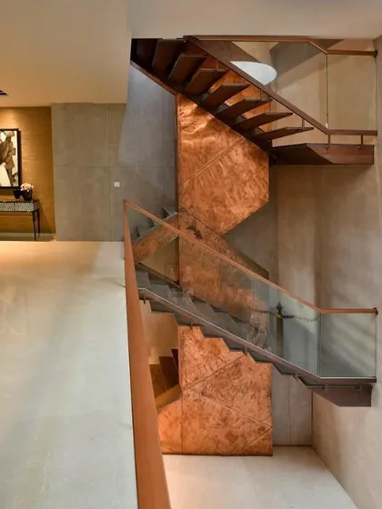 A full view of the Sainik Farms staircase, showing how it connects multiple levels of the home. The design is both a functional element and a vertical sculpture, with the glass balustrade ensuring it remains visually light.