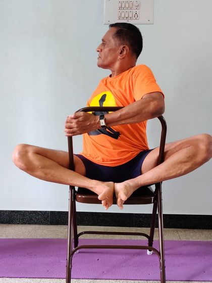 A seated Baddhakonasana (Bound Angle Pose) on a chair. This variation helps to open the hips and groin area while maintaining an upright, extended spine.