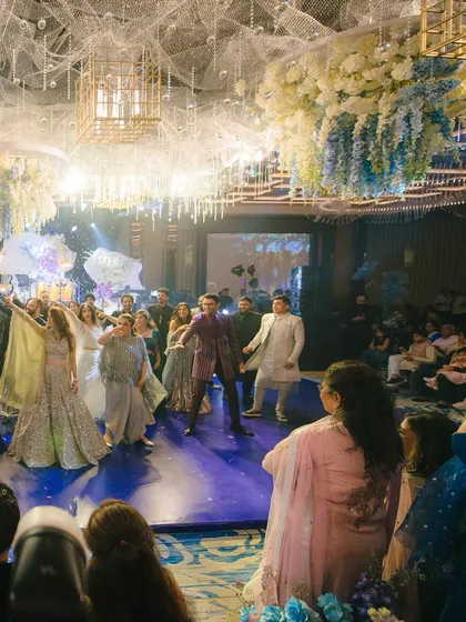 A wide shot of the dance floor, filled with guests enjoying the performances. The ceiling decor with hanging florals and crystals adds to the luxurious feel of the event.