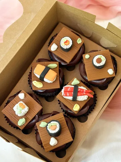 A unique set of six chocolate cupcakes designed to look like sushi. Each cupcake is topped with a detailed, handmade fondant creation, including maki rolls, nigiri, and ebi shrimp, showcasing a creative and playful theme for adult celebrations.