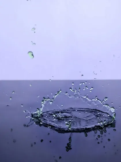 A minimalist yet captivating shot of a water droplet creating a perfect crown splash on a dark surface, showcasing technical skill in high-speed photography.