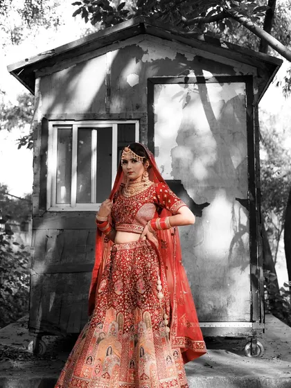 A unique color-splash portrait where the bride in her red lehenga stands out against a black and white background. This artistic choice makes the bridal attire pop.