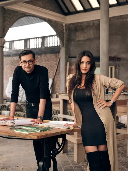 A portrait of us, Farah Ahmed and Dhaval Shellugar, the founders of FADD Studio. We are standing in a workspace that reflects our design ethos: a blend of raw materials, clean lines, and artistic focus.