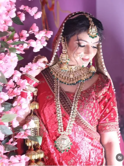 A bride posing next to pink blossoms, her red lehenga and heavy jewellery creating a striking contrast. This image highlights the complete bridal ensemble.