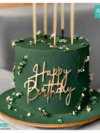 This sophisticated birthday cake features a deep forest green frosting, flecks of edible gold leaf, and a modern, gold acrylic 'Happy Birthday' topper. It's a perfect example of a chic and elegant design for an adult celebration.