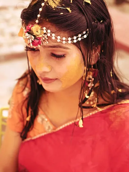 A serene portrait of the bride during her Haldi, with turmeric paste on her face and beautiful floral jewelry.