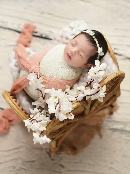 A newborn rests in a decorative wooden prop, surrounded by white flowers. I use a variety of props to create unique and artistic compositions for each baby's photoshoot.