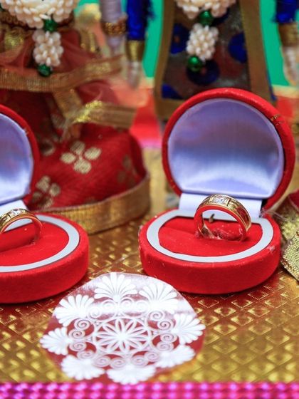 A close-up of the wedding rings in their boxes, set against a backdrop of traditional dolls representing the ceremony.