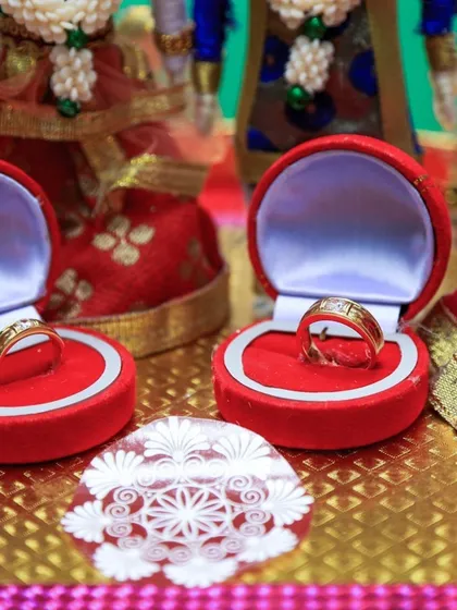 A close-up of the wedding rings in their boxes, set against a backdrop of traditional dolls representing the ceremony.