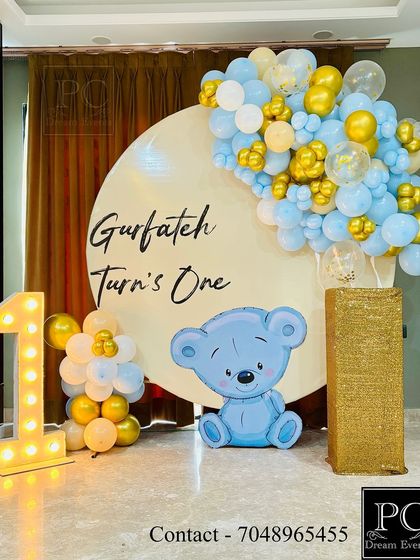 The soft lighting on the teddy bear birthday decor creates a warm and inviting atmosphere. The gold and blue balloons add a touch of elegance to this sweet and classic first birthday theme.