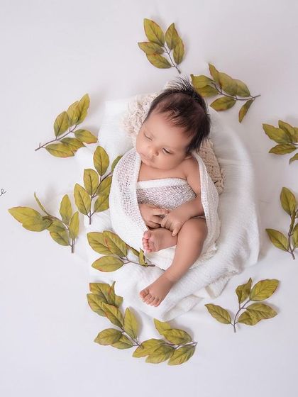 Nature's little miracle. A baby wrapped in white, surrounded by a circle of green leaves. The simplicity of this composition is what makes it so striking.