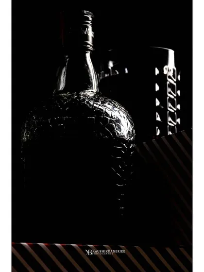 A fine art approach to liquor photography, using shadows and rim lighting to outline the distinct shape of a whiskey bottle and shaker. This style creates a sophisticated and mysterious feel.