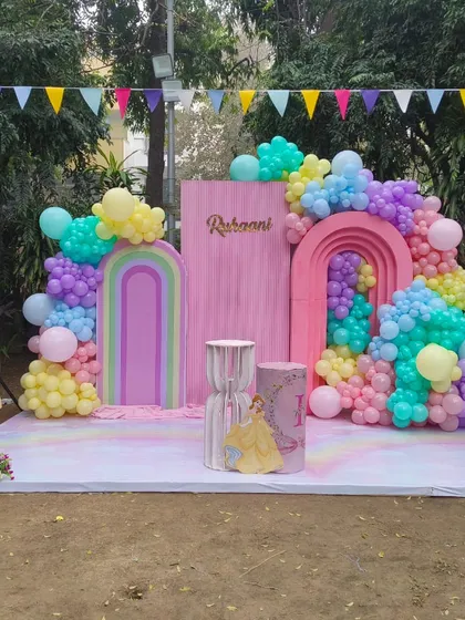 A full view of an outdoor princess party stage featuring Belle and Aurora cutouts, a pastel rainbow backdrop, and a number '3' prop.
