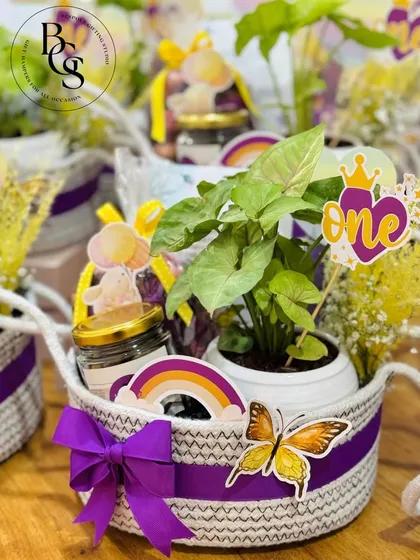A delightful return gift hamper for a first birthday party. This basket includes a small plant, cookies, and other themed goodies, making it a fun and memorable thank you for your little one's first big celebration.