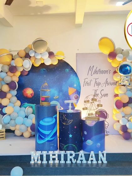 A "First Trip Around the Sun" space-themed birthday. This setup features a galaxy backdrop, astronaut cutouts, and a balloon arch with planet details.