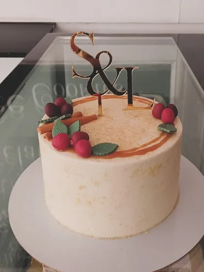 An anniversary cake with custom initials, decorated with cinnamon sticks and fondant cherries for a rustic, warm feel.