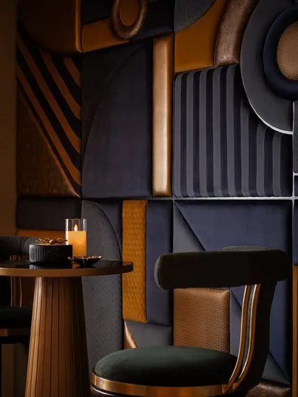 A close-up of the Art Deco-inspired fabric wall panel. This piece is a complex puzzle of different fabrics, textures, and shapes, all meticulously wrapped and assembled to create a single, dramatic piece of wall art that defines this corner.