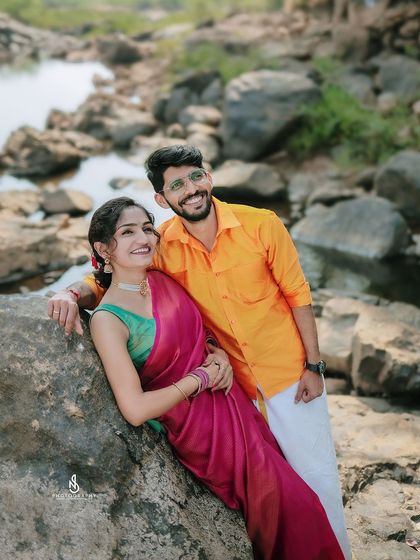 A joyful portrait, leaning against a large rock by the water. Their bright smiles and colorful attire radiate happiness.