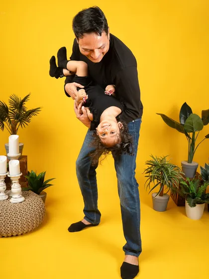 Let's have some fun! A father's playful moment with his daughter, full of laughter and joy. These candid shots against a vibrant yellow backdrop show the energetic and happy side of family life.