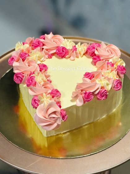 A heart-shaped cake decorated with a border of pink and cream buttercream rosettes.
