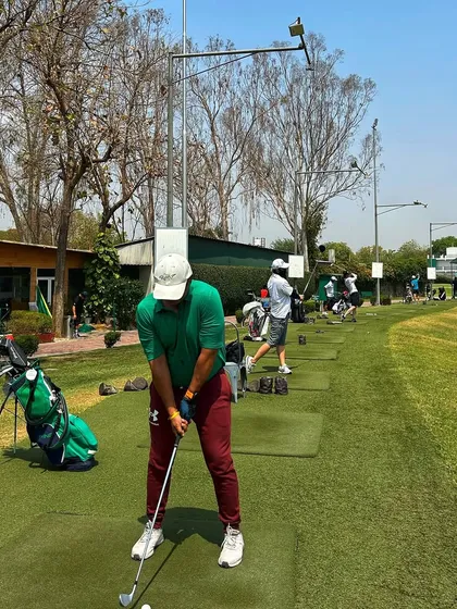 A golfer in a green shirt lines up his shot on the mat, with a full range of players behind him.
