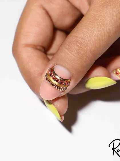 A unique jewellery design placed at the cuticle, using gold beads and red crystals.