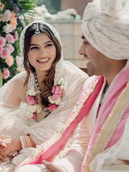 A quiet, happy moment after the Varmala exchange. The couple shares a laugh, their faces glowing with happiness, surrounded by beautiful floral decor.
