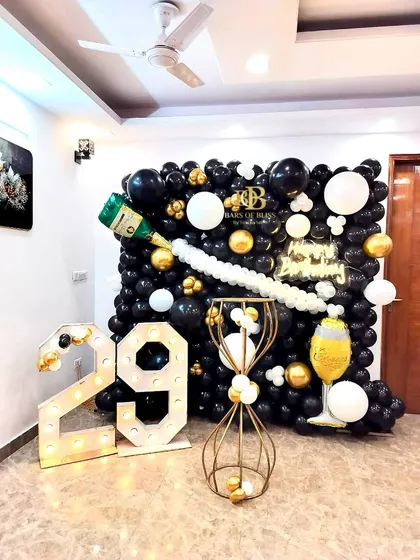 A sophisticated champagne-themed birthday party. This unique setup includes a wall of black, white, and gold balloons with a champagne bottle balloon pouring out "bubbly" white balloons, complemented by '29' marquee numbers.