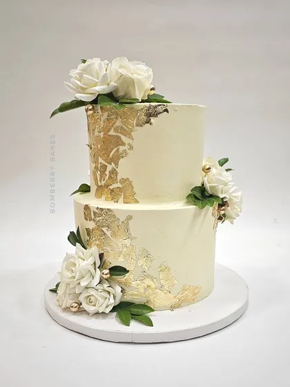 Another angle of the elegant two-tier white and gold cake, showing the placement of the sugar flowers and gold leaf.