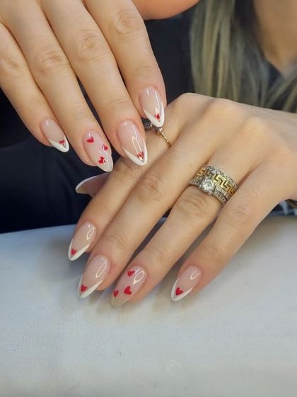 A delicate and romantic design on stiletto nails, featuring a modified French tip and tiny, hand-painted red hearts.