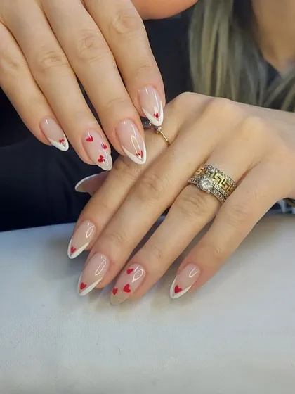 A romantic take on the French manicure with delicate V-shaped tips and tiny red hearts scattered on a nude base.