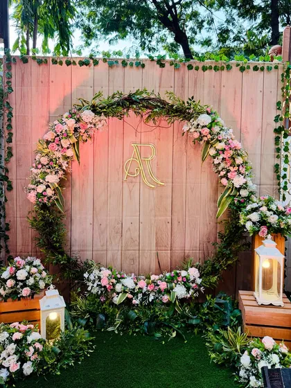 A rustic-chic photo booth with a large wreath of greenery and pastel flowers. The couple's initials monogram in the center adds a personalized touch to the wooden backdrop.