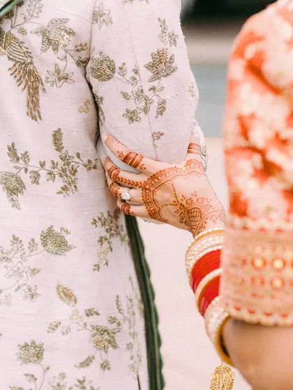The magic is always in the details. A close-up of the bride's intricate mehendi and traditional red choora as she holds the groom's arm, showcasing the beautiful embroidery on his Jayanti Reddy sherwani. These are the moments and details I live for.