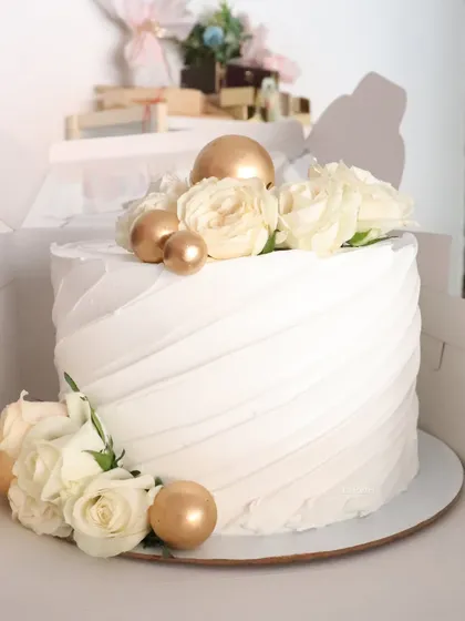 Simple, elegant, and so pretty. This single-tier cake features a diagonal textured buttercream, adorned with white roses and shiny gold spheres.