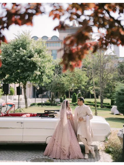 A stylish, candid moment in Turkey. The couple stands by a classic white convertible, sharing a look, framed by lush greenery and autumnal leaves.