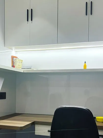 A look at a newly completed study room in Noida. The design features a clean, modern aesthetic with white overhead cabinets, a wood-finish desk, and integrated LED lighting. The vertical fluting on the wall adds a subtle textural detail.