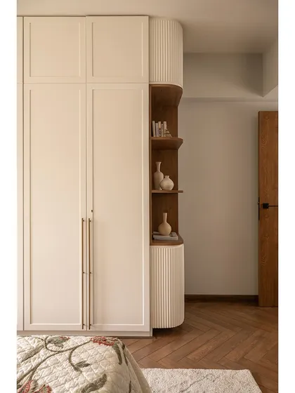 In this guest bedroom, we integrated a mandir within the wardrobe. The design features clean lines, with curved corner shelving in a warm wood tone that contrasts beautifully with the white wardrobe doors.