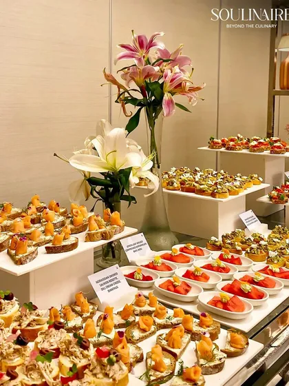 A vibrant and elegant display of our gourmet canapés, featuring a variety of textures and flavours like smoked salmon crostini and tomato tarts. This spread, accented with fresh lilies, showcases our dedication to artisanal food presentation.