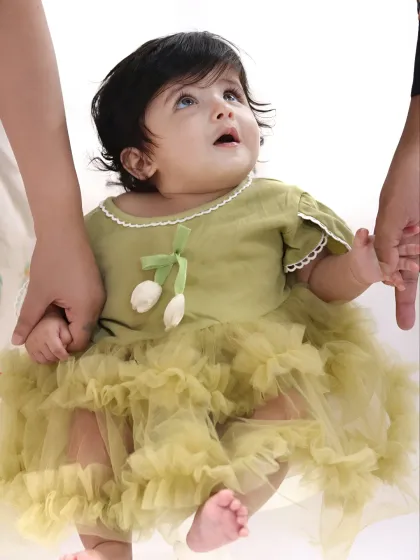 A close-up of a beautiful baby girl in a lovely green dress, securely held by her parents' hands. This shot highlights the delicate details and innocence of infancy.