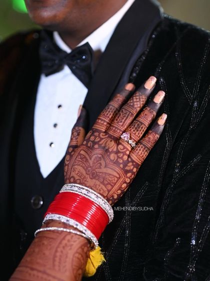 The bride's hand on the groom's shoulder, a classic shot that beautifully displays the intricate mehendi stain and bridal bangles.