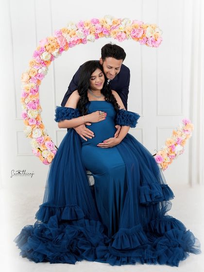 A beautiful couple portrait with a floral moon prop. The deep blue gown and the romantic pose create a dreamy and elegant scene, perfect for celebrating their journey.