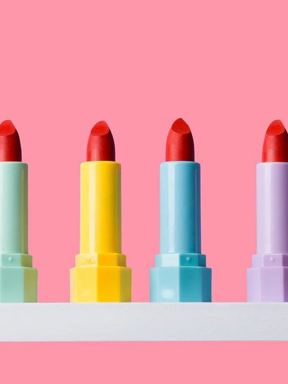 A row of colorful lipsticks against a solid pink background. This simple, vibrant, and playful composition is perfect for social media and beauty blogs.